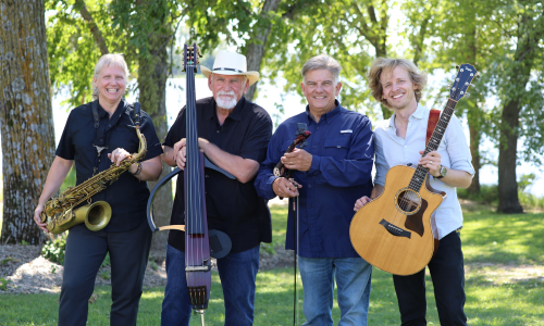 Four people outdoors with musical instruments: saxophone, standing bass, microphone, and guitar, standing in a grassy area with trees.
