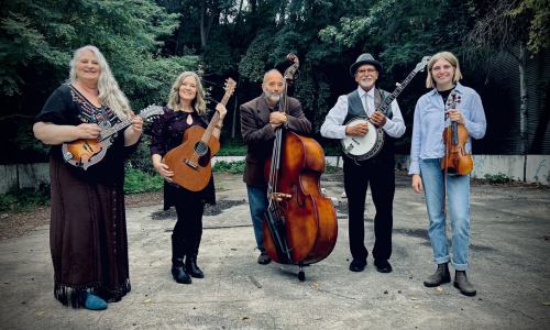 Five people holding different musical instruments stand in an outdoor setting with trees in the background.