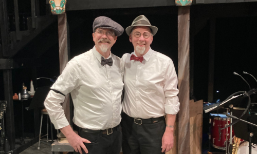 Two men in white shirts and bow ties standing on a stage.